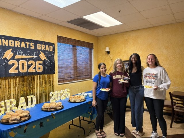 Four Class of 2026 graduates at the Shrine Club's reception holding plates of food in front of the Congrats Grad banner.